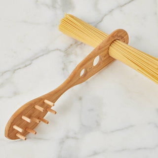 Wooden pasta server with holes holding a bundle of uncooked spaghetti on a marble surface