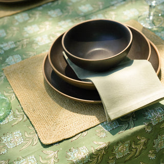 Set of black ceramic bowls on a green patterned tablecloth with a glass and napkin.