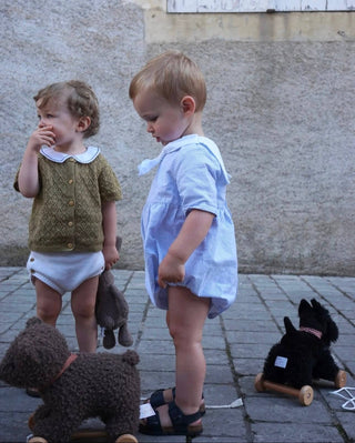 Two young children standing on a stone pavement with toy dogs, wearing casual clothing.