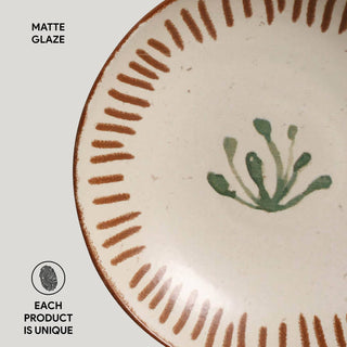 Ceramic plate with green plant design and brown reactive glaze on a white background