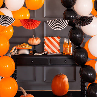 Halloween-themed table setting with balloons, pumpkins, and decorative items against a dark wall.