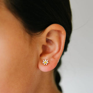 Close-up of an ear wearing a daisy flower earring with a blurred background