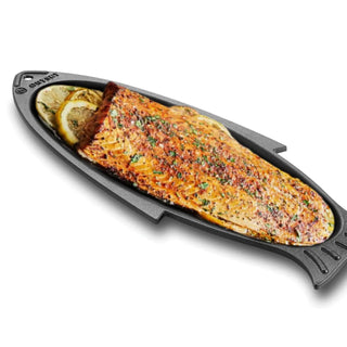 Grilled salmon on a black grill pan with lemon slices on a white background