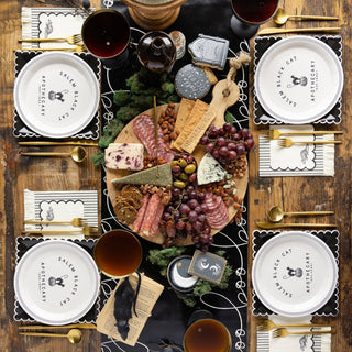 Gourmet platter with assorted meats, cheeses, and fruits on a wooden table with wine glasses and place settings.