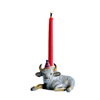 Ceramic bull figurine with a birthday hat and lit red candle on a light blue background