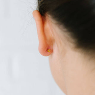 Close-up of an ear with a gold earring on a light background