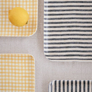 Textile swatch with yellow checkered pattern, lemon, gray and white striped pattern on a neutral background.