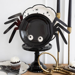 Spider-shaped plate holder with black and white design on a table with Halloween-themed decor.