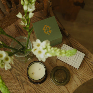Candle, flowers, and a green box on a wooden surface