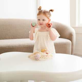 Child holding colorful objects in a bright room with a couch and table.