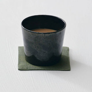 Black ceramic cup on a green coaster with a white background