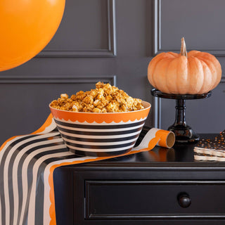 Bowl of popcorn on a striped tablecloth with pumpkins and balloons against a gray wall.