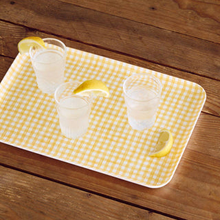 Three glasses of lemonade on a yellow checkered tray with lemons on a wooden surface