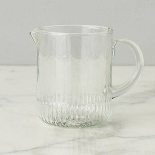 Clear glass pitcher on a marble surface with a light gray background