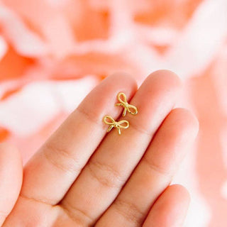 Gold bow-shaped earrings held between fingers against a blurred background