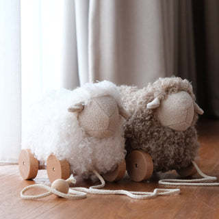 Two fluffy sheep toys with wooden legs on a wooden floor.