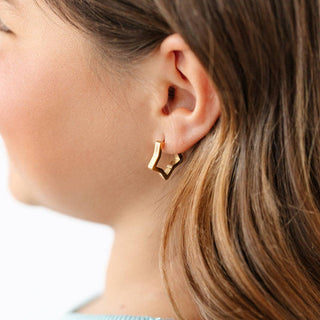 Close-up of a person wearing a gold geometric earring with a blurred background