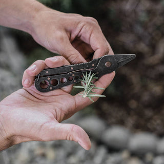 Person holding a multi-tool with a small plant, outdoors.
