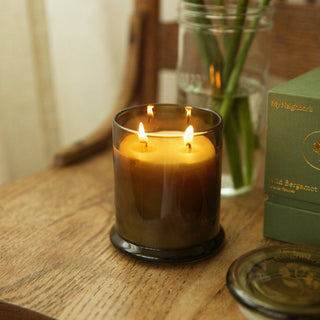 Candle with two flames on a wooden surface next to a vase and a box.