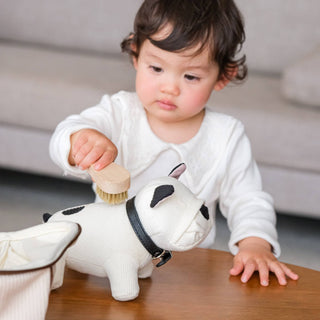 Child playing with a plush dog toy and brush on a wooden surface.
