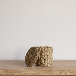 Woven basket with a lid on a wooden surface against a plain background