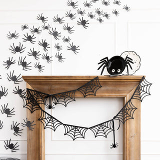 Halloween decorations including spider webs and black spiders on a white wall.