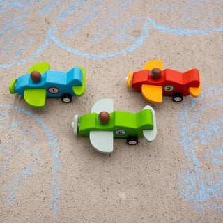 Three colorful toy cars on a textured surface with chalk drawings.