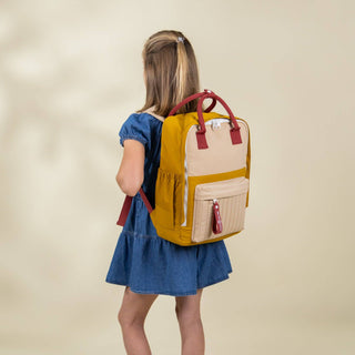 Girl wearing a yellow and beige backpack on a beige background