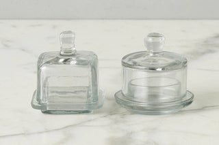 Two clear glass containers with lids on a marble surface