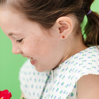 Close-up of a young girl holding a red flower against a green background