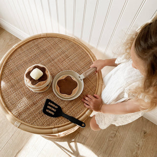 Child playing with toy kitchen set on a round wicker table