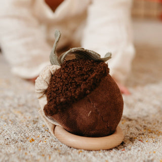 Brown felt acorn toy on a sandy surface