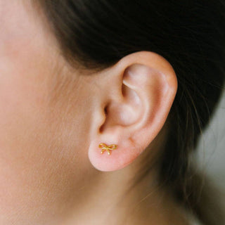 Gold bow-shaped earring on a person's ear with a neutral background