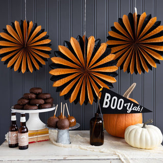 Halloween-themed decor with paper fans, pumpkins, and 'BOO Yah!' banner against a dark wooden panel background.