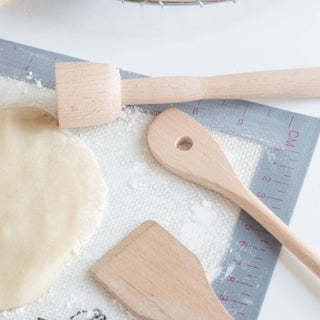 Wooden kitchen utensils on a surface with a cookie and cooling rack in the background.
