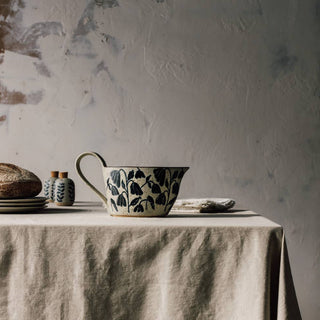 Table setting with a floral-patterned teacup on a textured tablecloth against a textured wall.