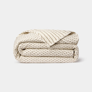 Folded beige quilt with leaf pattern on a white background