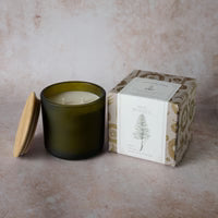 Green candle in a glass jar with a wooden box on a beige surface