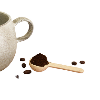Ceramic mug with coffee beans and a wooden scoop on a wooden surface.