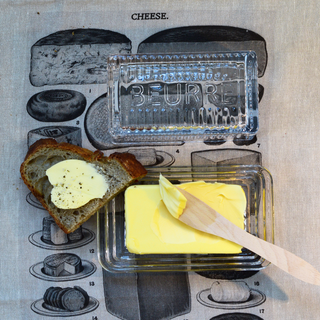 Butter dish with a stick of butter, a slice of bread with butter, and a wooden knife on a vintage-style background.