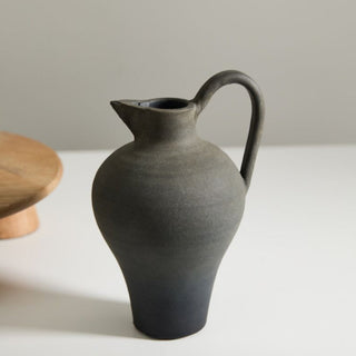 Black ceramic pitcher on a white surface with a neutral background