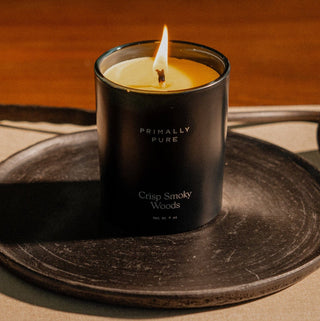 Black candle in a holder labeled 'Primally Pure' on a wooden surface.
