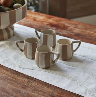 Set of ceramic mugs on a wooden table with a striped cloth