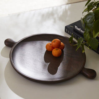 Wooden tray with oranges on a white surface next to a book and plant