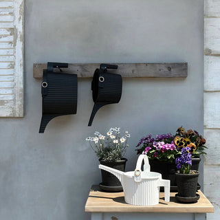 Wall-mounted planters with a wooden shelf and potted plants on a table against a gray wall.