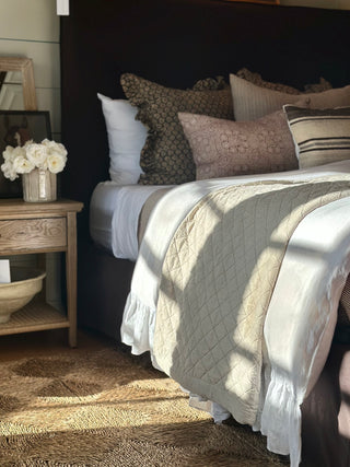 Bedroom with a bed featuring patterned pillows and a quilt, next to a wooden nightstand with decorative items.