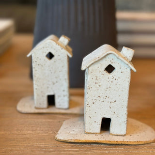 Two small ceramic house models on a wooden surface with a blurred background.