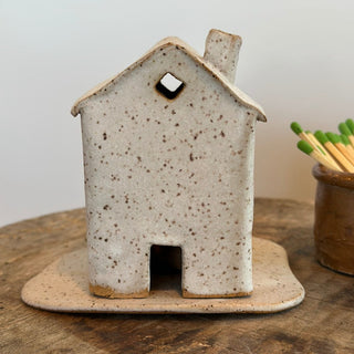 Ceramic house-shaped object on a wooden surface with a plain background