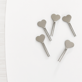 Five silver metal heart-shaped picks with straight pins, arranged on a clean white surface.