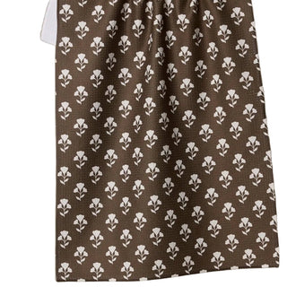 Brown towel with white floral pattern hanging on a line, with cups and saucers below.